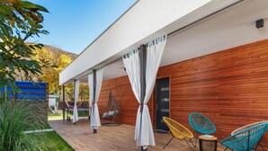 Un espace extérieur abrité, doté d’un plancher en bois, d’un fauteuil suspendu et de deux chaises colorées.