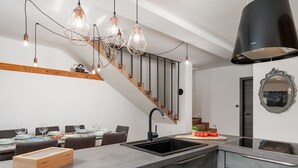 Une cuisine moderne dotée d’un îlot central, d’un coin repas avec un escalier et d’un éclairage suspendu.