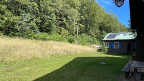 A grassy yard with a wooden bench and a building with a green roof. - Chalet Le Clapotis by Interhome (Le Lieu)