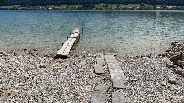 A wooden pier extending into a calm lake with a rocky shore and a backdrop of green hills. - Chalet Le Clapotis by Interhome (Le Lieu)