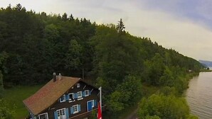 A house with a red and white flag, a car parked in front, and a river nearby. - Chalet Le Clapotis by Interhome (Le Lieu)