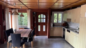 A spacious kitchen with wooden cabinets and a dining area with a table and chairs. - Chalet Le Clapotis by Interhome (Le Lieu)