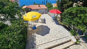 A patio area with outdoor furniture and umbrellas, a stone floor, and a view of the sea and mountains in the background. - Wohnung mit Terrasse, Grill, Parkplatz by Interhome (Novi Vinodolski)