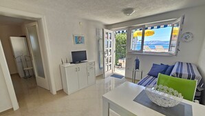 A modern living room with a sofa, a dining table, and a TV on a cabinet. - Wohnung mit Terrasse, Grill, Parkplatz by Interhome (Novi Vinodolski)