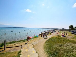 Une plage avec un chemin en béton menant à l’eau, entourée de pelouses et de parasols.