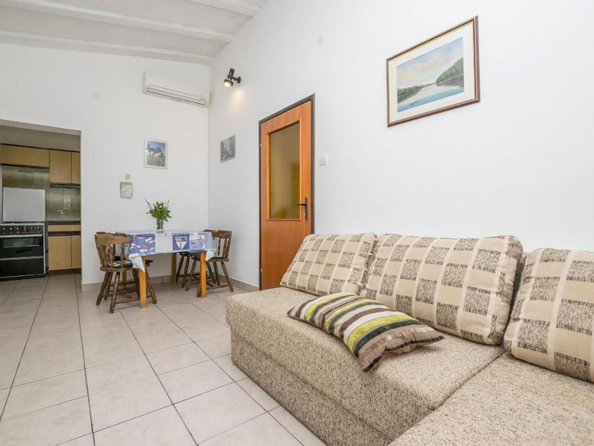 Zona d'estar acollidora amb un sofà, una taula de dinar amb cadires i una cuina al fons.
