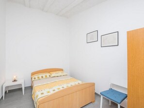 Une chambre avec un lit en bois, une petite table de chevet avec une lampe, un banc bleu et deux tableaux encadrés accrochés au mur.