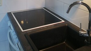 Une cuisine dotée d’une plaque de cuisson à induction noire, d’un évier en acier inoxydable et d’une hotte aspirante au-dessus.