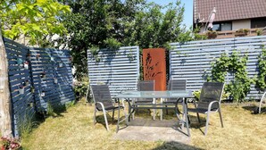 Une terrasse avec une table en verre et des chaises en métal, entourée d’une clôture en bois et agrémentée de plantes en pot.