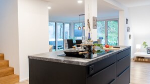 Una cocina moderna con una isla grande, suelo de madera y ventanas amplias que dan al exterior.