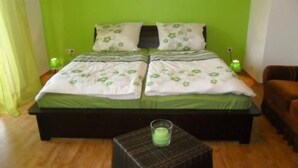 Un letto matrimoniale con biancheria verde, un comodino con una candela verde e una poltrona marrone.