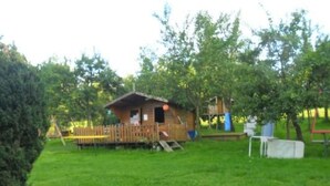 Una baita di legno con una veranda, immersa in un prato erboso e circondata da alberi.