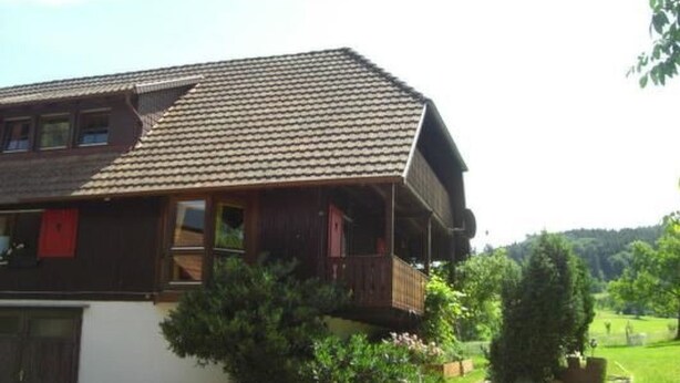 Una casa in legno tradizionale con tetto spiovente, un balcone e un vialetto che conduce verso un paesaggio verde.