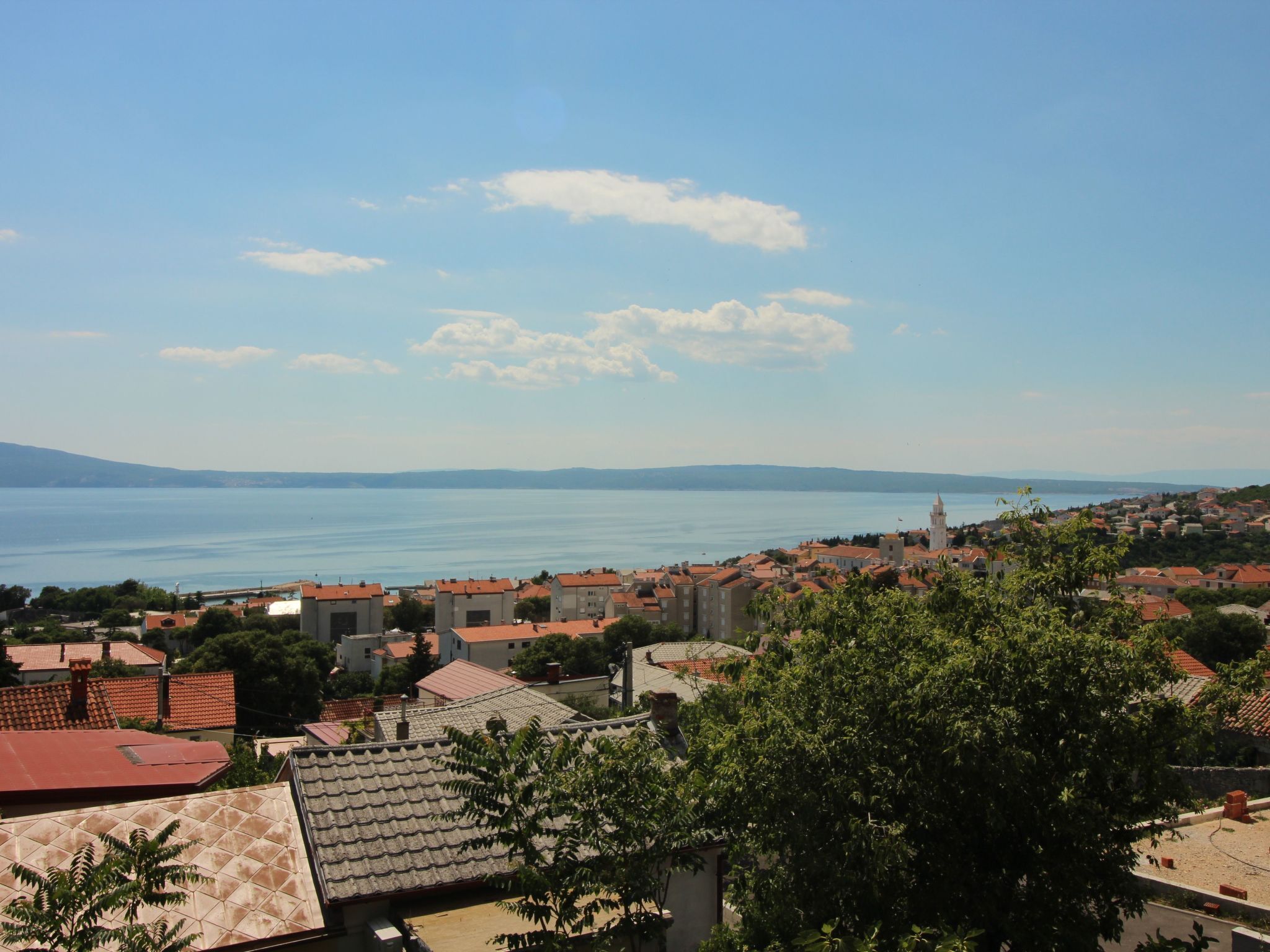 Eine Küstenstadt mit roten Dächern, einem markanten Turm und Blick auf das Meer.