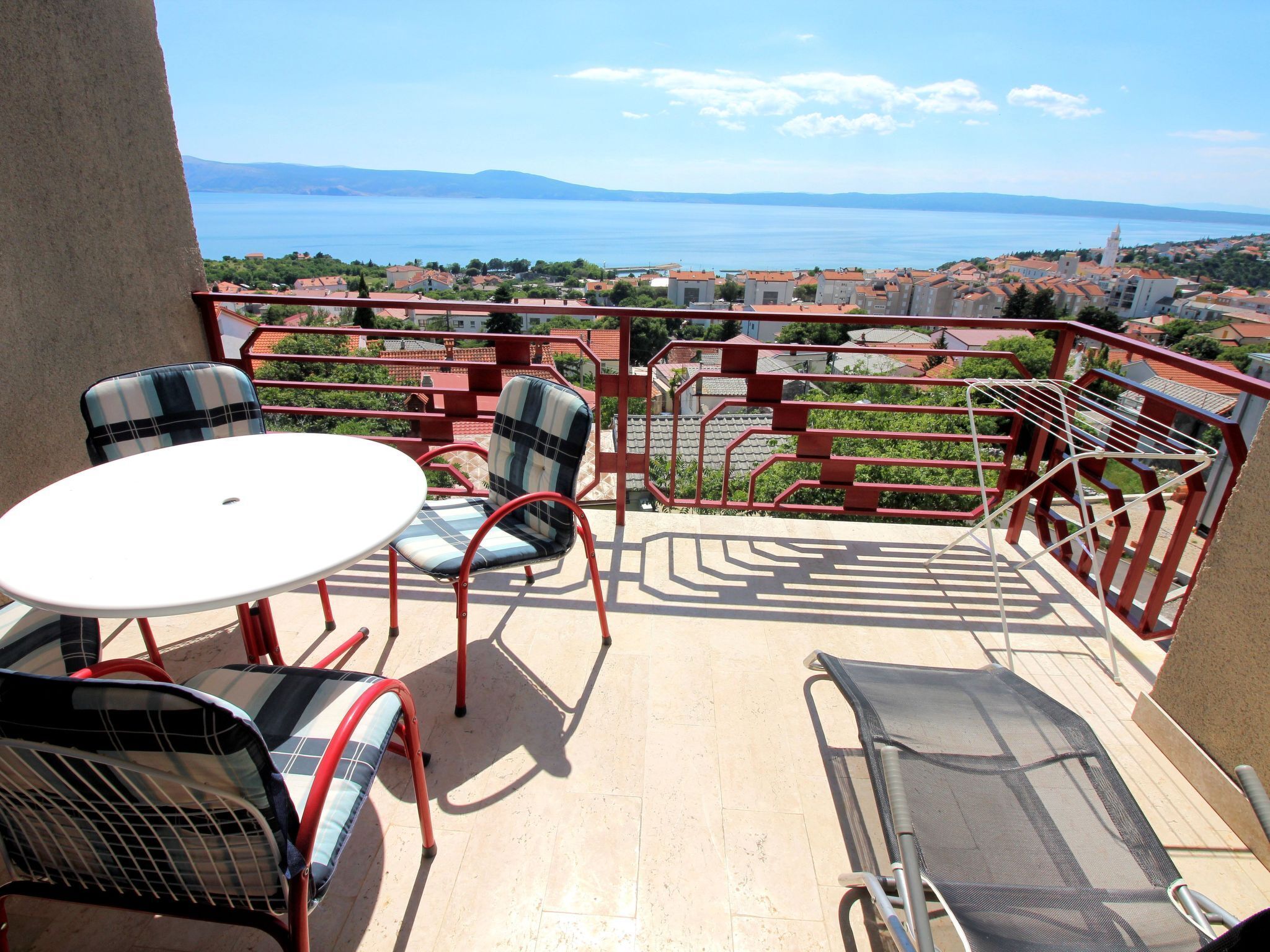 A balcony with a table and chairs, offering a view of a coastal town and the sea.
