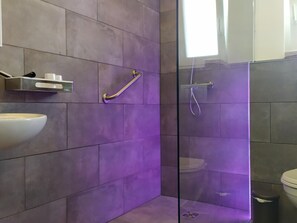 Ein modernes Badezimmer mit einer Duschkabine aus Glas, einem weißen Waschbecken und einer Haltestange.