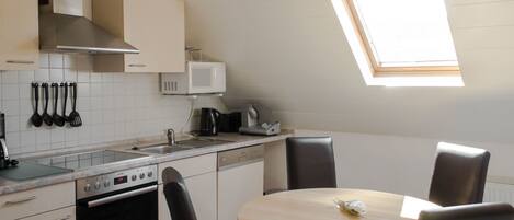 A modern kitchen with a microwave, stove, and sink. There is a round table with chairs and a skylight above.