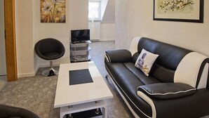 Un salon moderne avec un canapé en cuir noir et blanc, une table basse blanche, un fauteuil noir et un téléviseur posé sur un meuble.