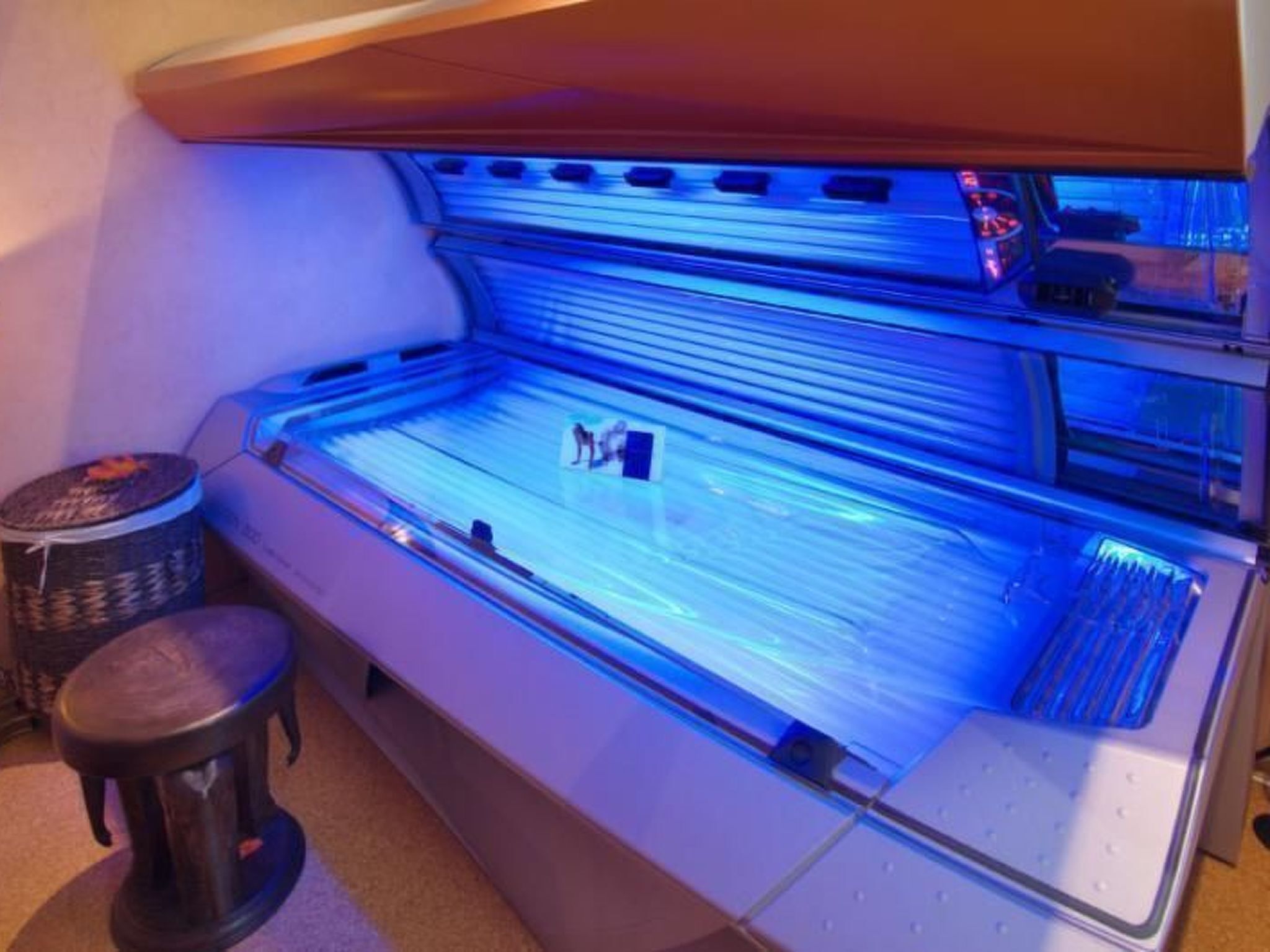 A tanning bed with a glass enclosure and a stool.