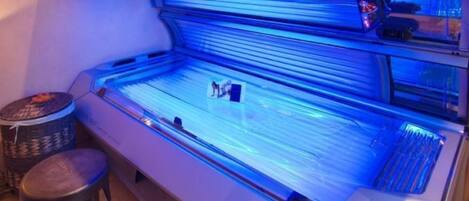 A tanning bed with a glass enclosure and a stool.