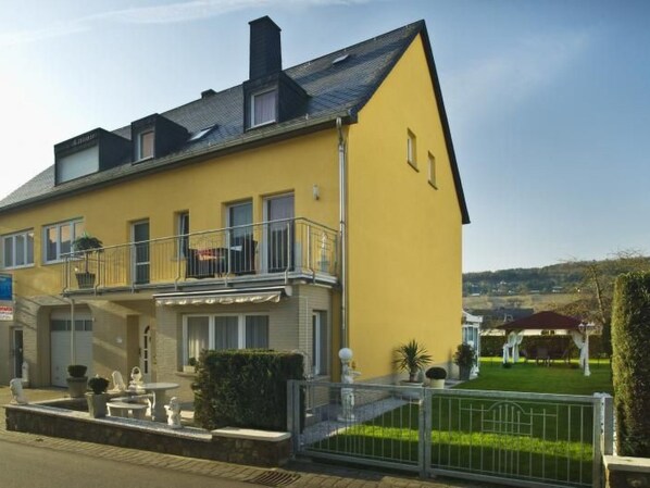 A yellow building with a balcony, a small garden, and a fence.