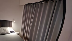 Een slaapkamer met een bed, gordijnen, een nachtkastje en een wandlamp.