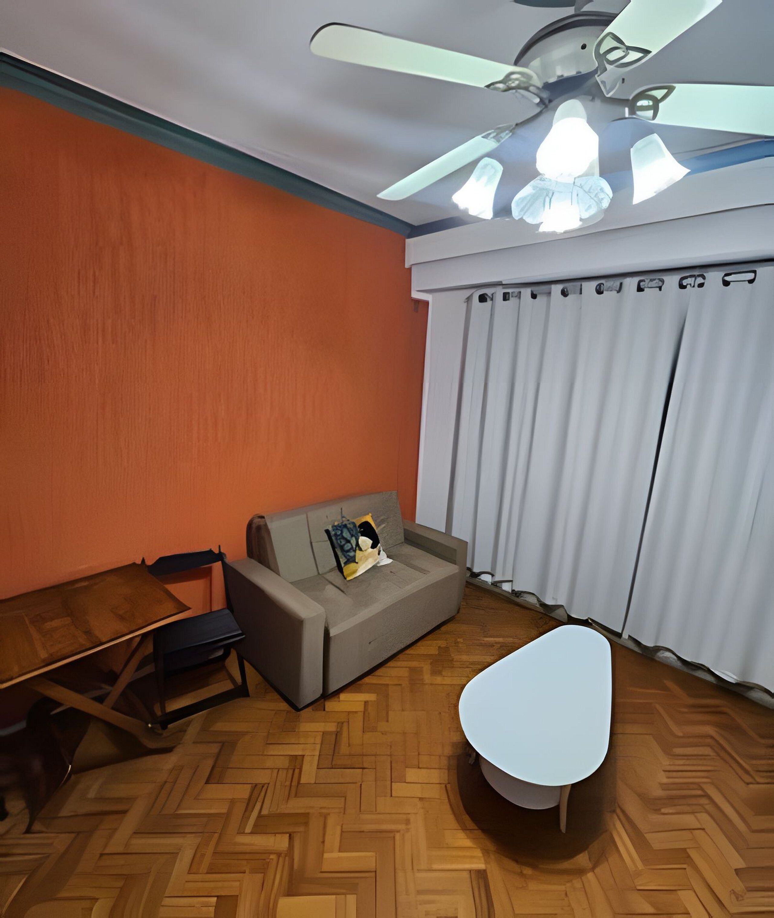 A room with a ceiling fan, a sofa, a small table, and a window with curtains.