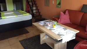 Et værelse med en seng, en sofa, et lille bord med en plante og en trappe.