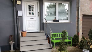 En hovedindgang med en hvid dør, en grøn bænk og en lille trappe til indgangen.