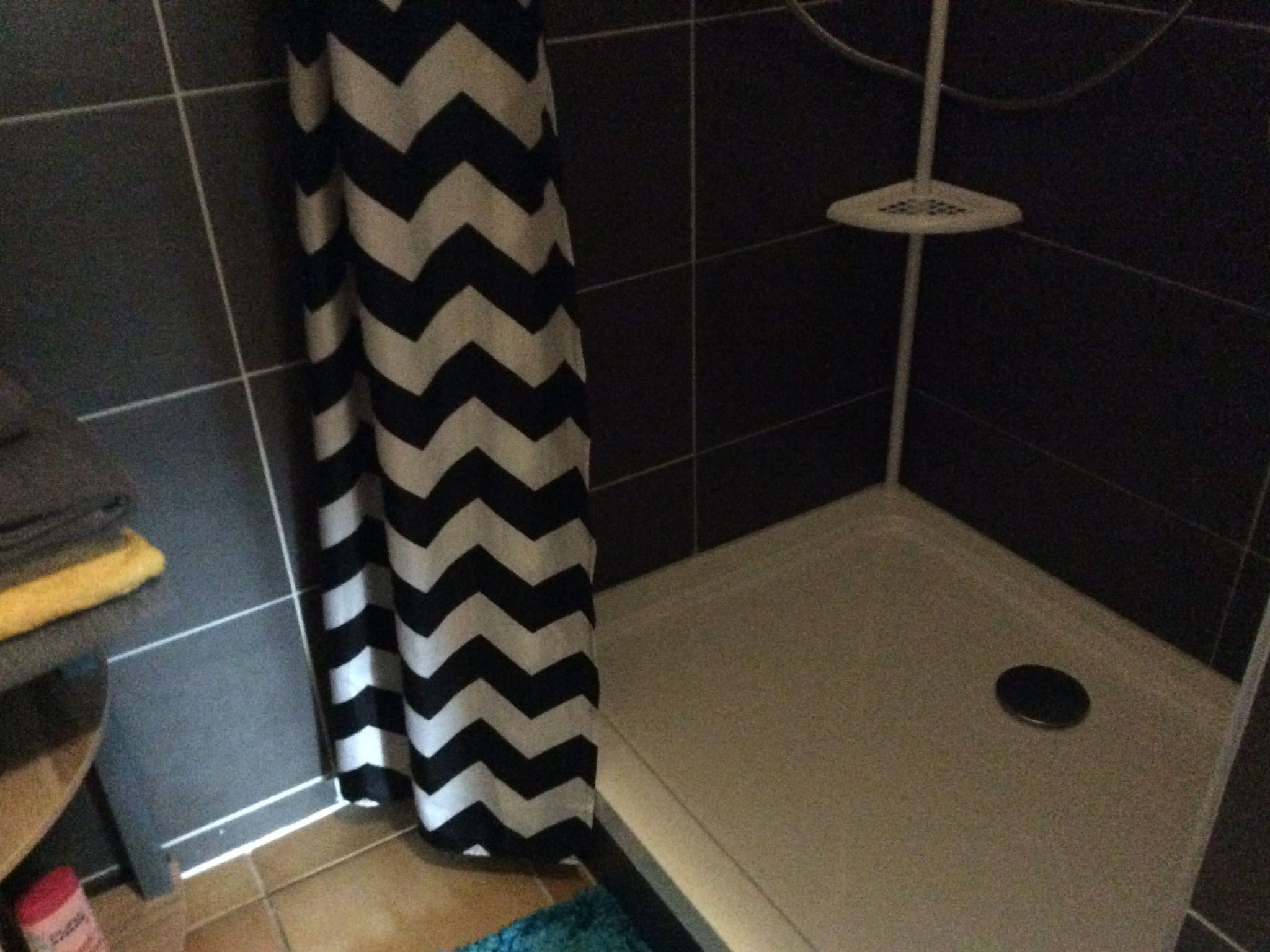 A small, enclosed shower area with a black and white chevron-patterned shower curtain, a white showerhead, and a tiled floor.
