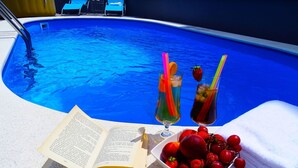 A poolside setting with a book, two drinks with straws, and a bowl of fruit. - apartment "Vila Veronique 7" by Interhome (Crikvenica/Dramalj)