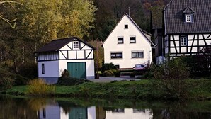 A traditional half-timbered house with a green door and a white facade, reflecting in a calm body of water. - Chalet Wiedfluh in Waldbreitbach by Interhome (Waldbreitbach)