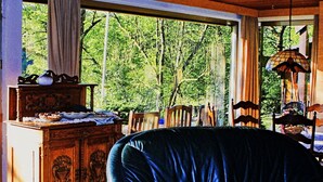 A room with a large window, a wooden cabinet, a blue chair, and a hanging lamp. - Chalet Wiedfluh in Waldbreitbach by Interhome (Waldbreitbach)