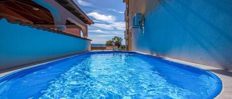 A swimming pool with a clear blue water surface, surrounded by a building with a tiled floor and a blue wall.