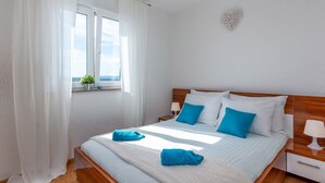 A bedroom with a large bed, white curtains, a window with a view, and a heart-shaped decoration on the wall.