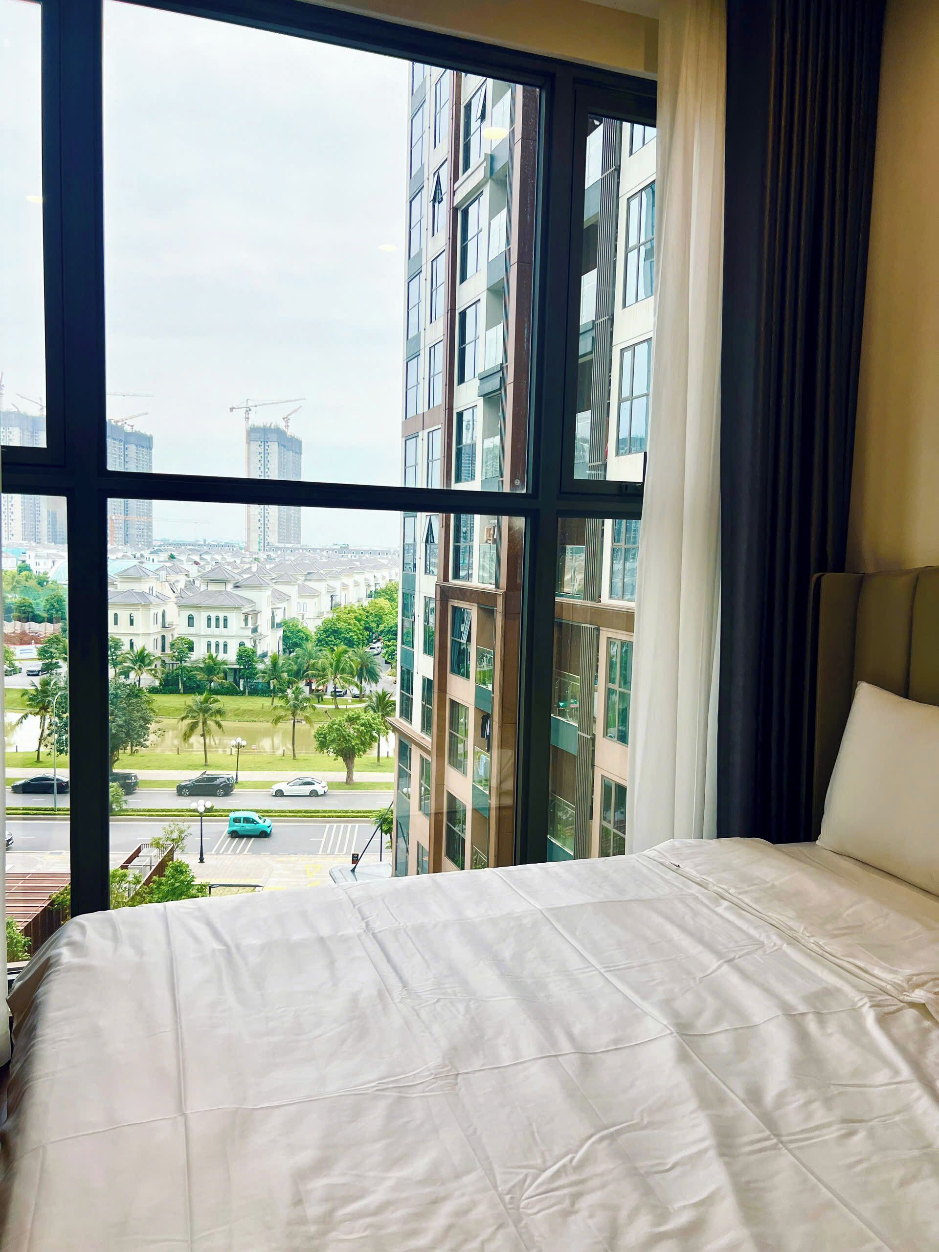 A hotel room with a large window, a bed, and a view of surrounding buildings.