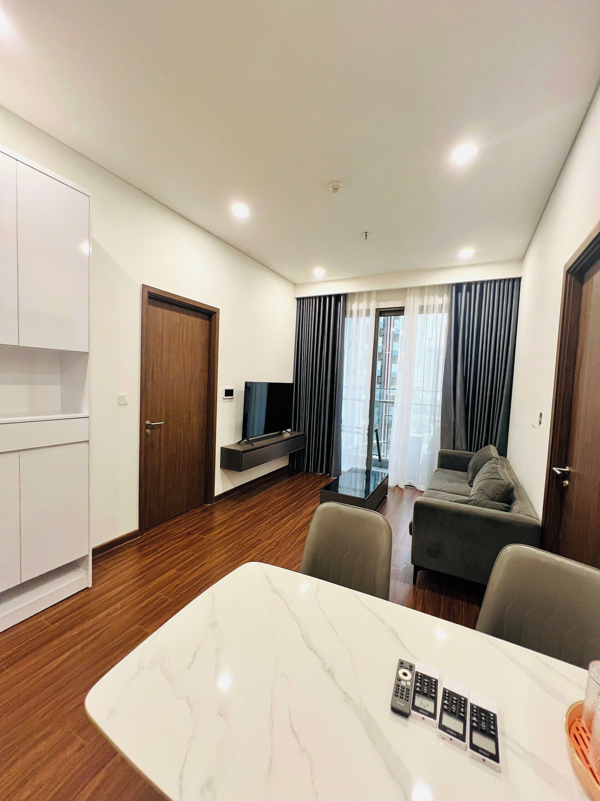 A modern living room with a sofa, a TV, a dining table with chairs, and a kitchen area with cabinets.