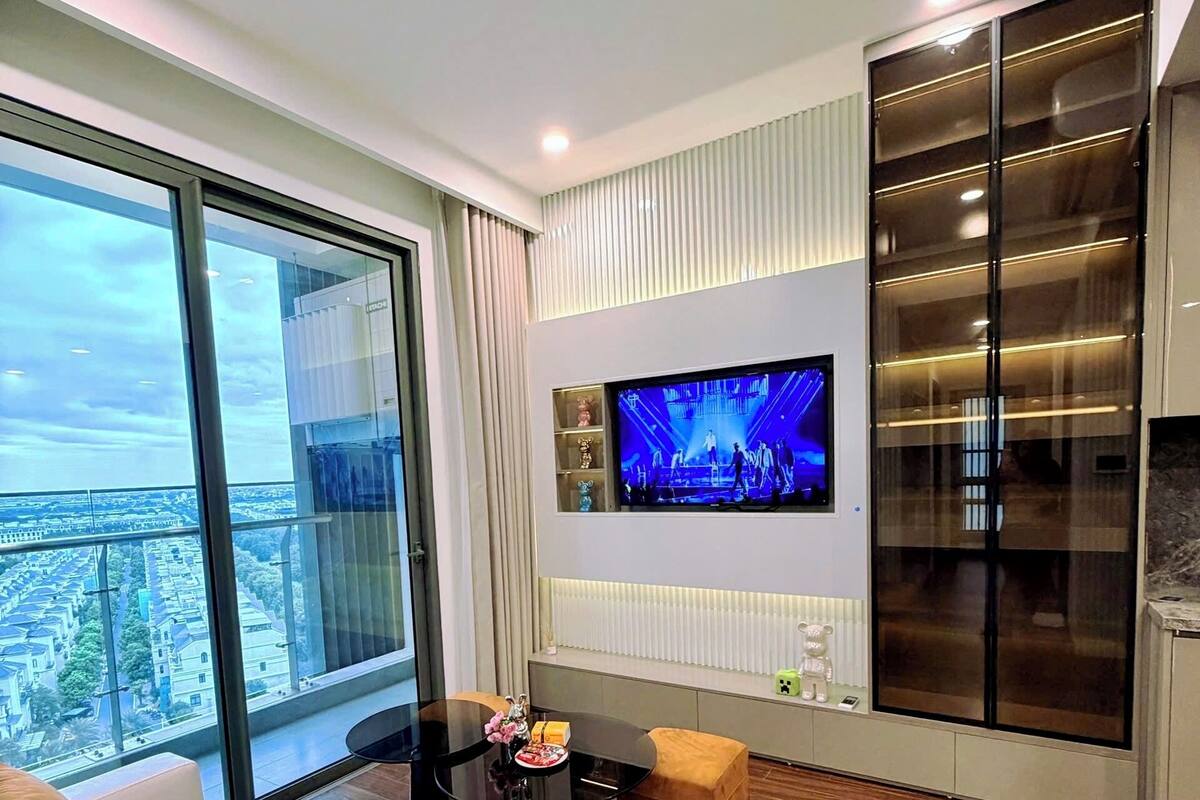 Ein modernes Wohnzimmer mit großem Fernseher, bequemen Sitzmöglichkeiten und Blick auf die Stadt.