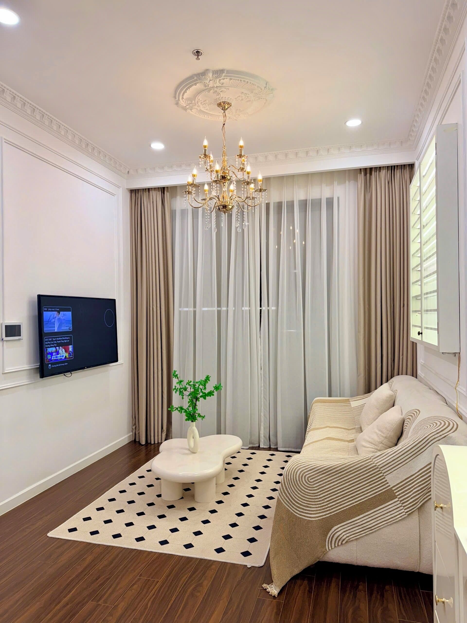 Een moderne woonkamer met een kroonluchter, een flatscreen televisie, een bank en een kamerbreed tapijt met een patroon.