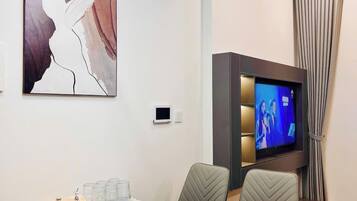 Una moderna camera d'albergo con un tavolo da pranzo in marmo, comode sedie, una TV a schermo piatto e un'opera d'arte contemporanea appesa al muro.