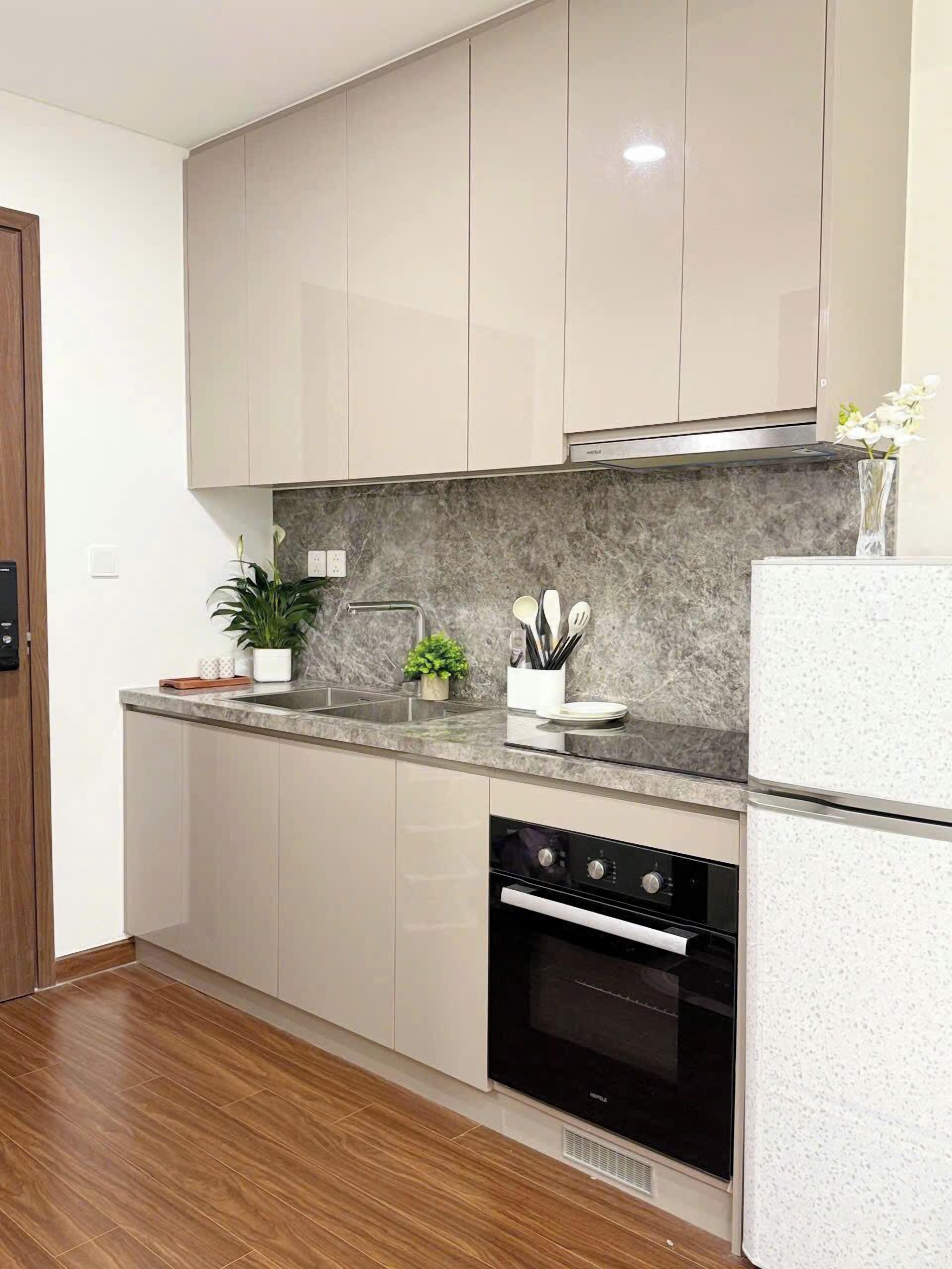 A modern kitchen with light-colored cabinets, a granite countertop, a built-in oven, and a stainless steel sink.