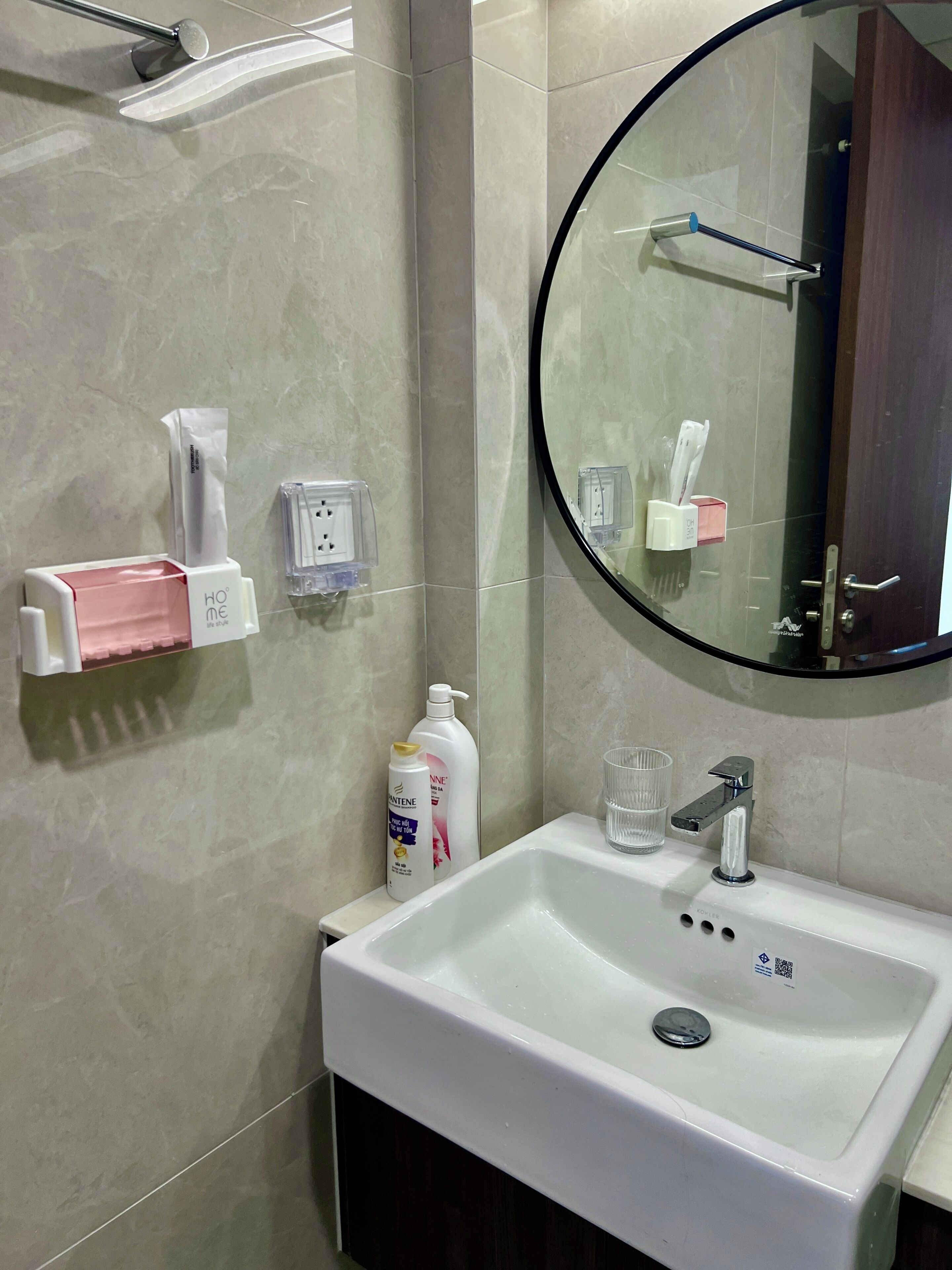A bathroom with a white sink, a mirror, a towel dispenser, a soap dispenser, and a glass.