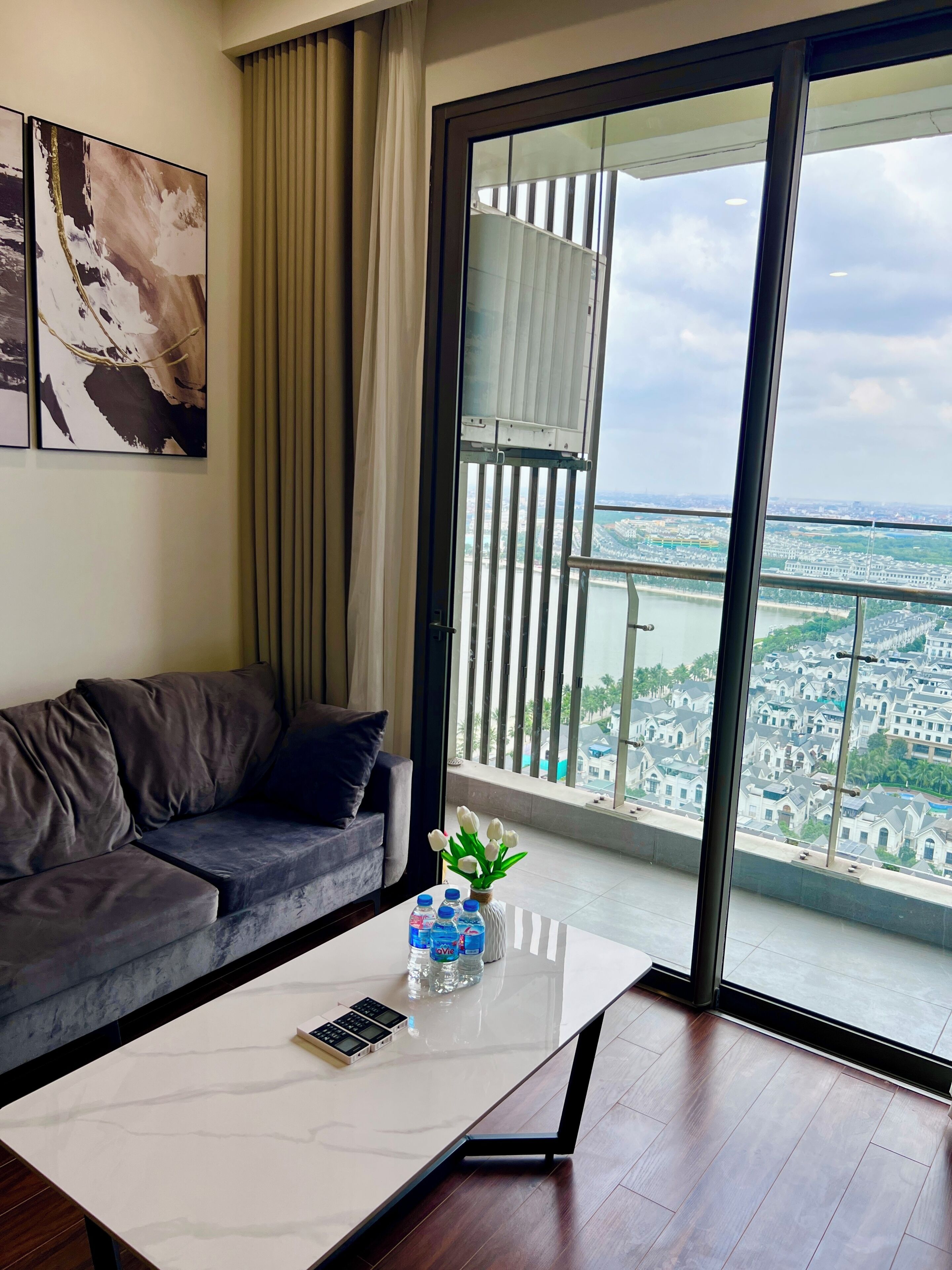 A modern living room with a grey sofa, a white coffee table, and a view of a cityscape through large windows.