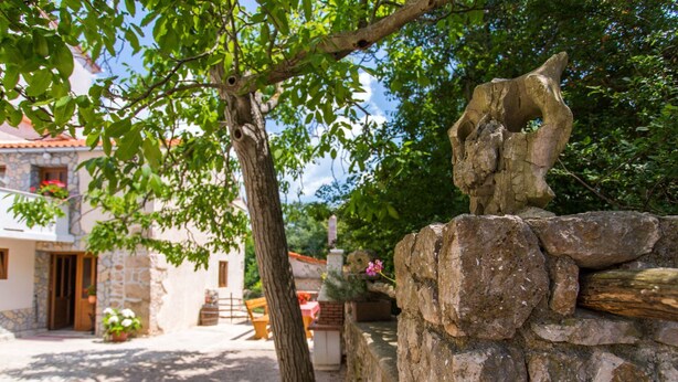 A stone bench with a carved animal figure, a tree, and a building with a stone facade and a door. - Gemütliches Steinhaus Nonna Stara by Interhome (Polje)