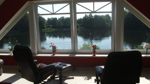 Une pièce dotée d’une grande fenêtre donnant sur un lac, de deux fauteuils et d’une petite table.
