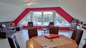 Un salon moderne avec un coin repas, des murs d’un rouge vif, de grandes fenêtres et une vue sur l’extérieur.