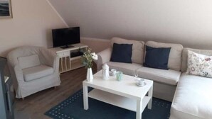 Een gezellige woonkamer met een bank, een klein bijzettafeltje, een televisie op een dressoir en een decoratieve vaas.