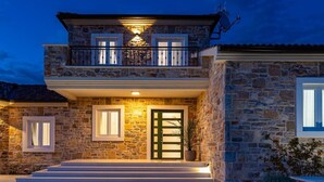 A two-story stone house with a balcony, a front door, and a small garden area.