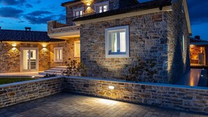 A stone house with a balcony, a satellite dish, and a well-lit entrance.
