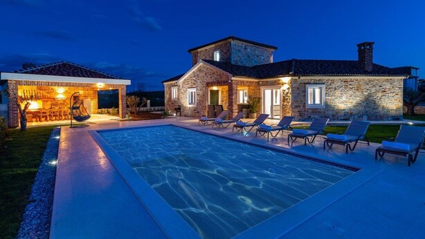 A stone house with a swimming pool and lounge chairs.